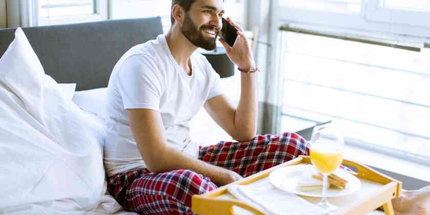 A man using a phone while having breakfast in bed